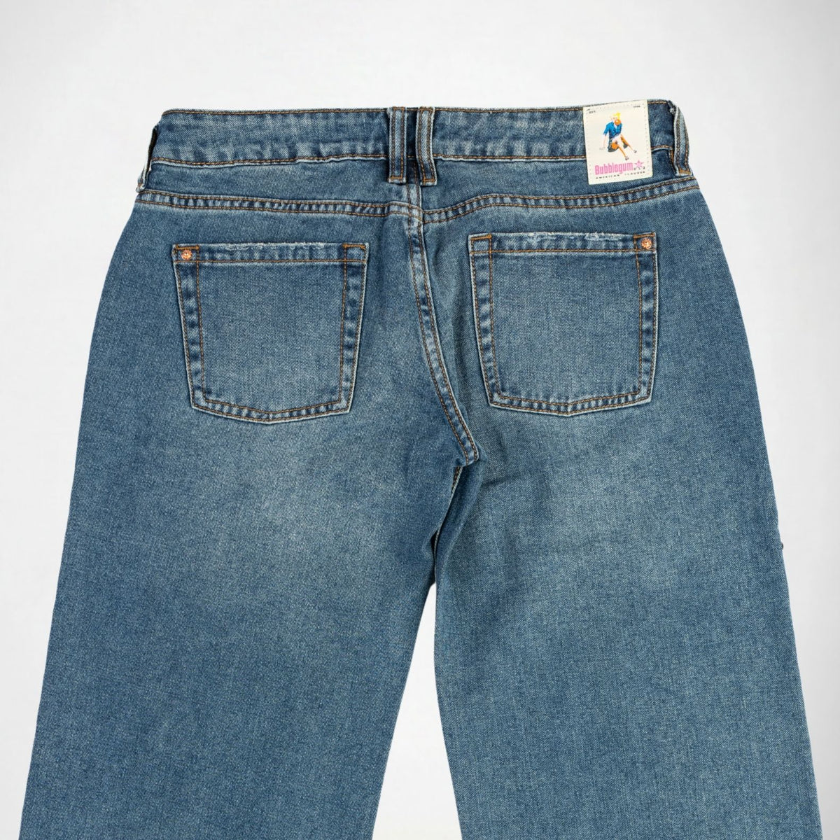 Back view of a pair of blue denim Bubblegum jeans on a light gray background, showing the waistband, belt loops, two rear pockets, and a small colorful brand tag near the back right waistband.