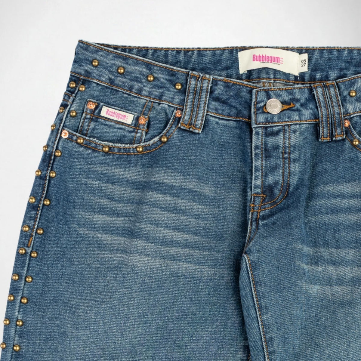 Close-up of a pair of blue denim Bubblegum jeans with a gold-tone studs along the pocket edges and waistband, shown against a plain light background.