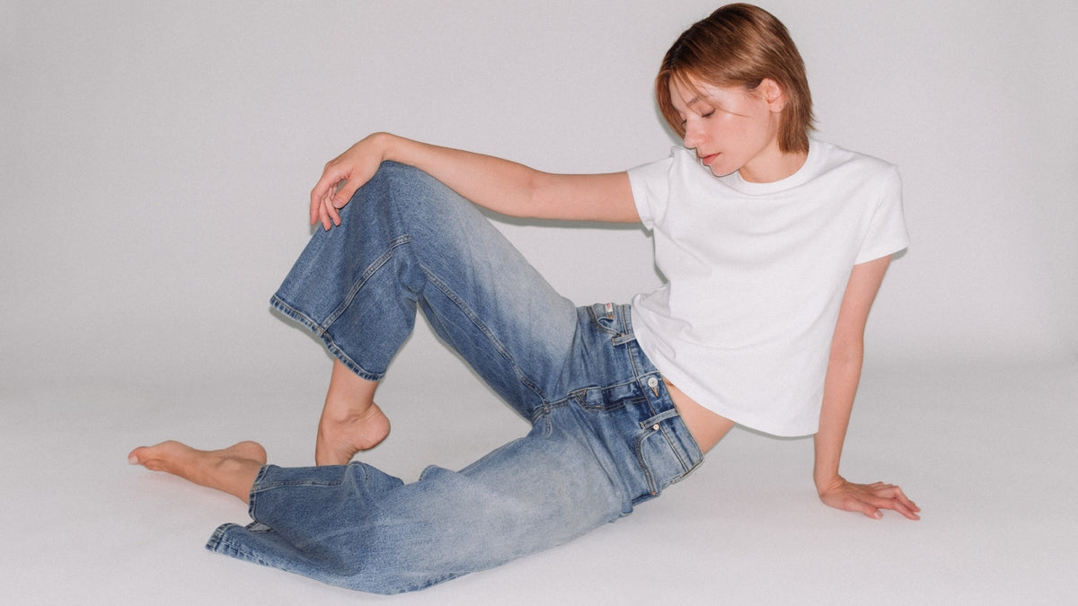 A model wearing a white t-shirt and light-wash blue Bubblegum jeans, posing on a seamless light gray studio background.