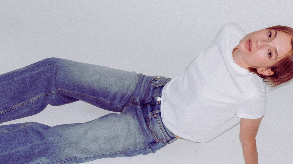 A model lying on their side wearing a white short-sleeve polo shirt and blue Bubblegum jeans against a plain light gray background.